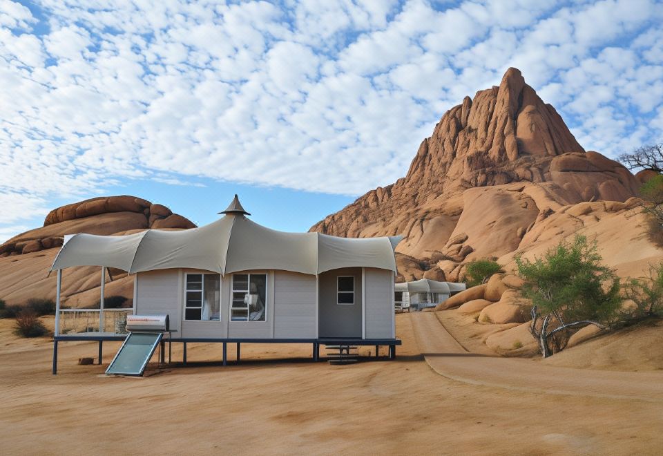 a tent - like structure is set up in a desert - like area with a sandy terrain and mountains in the background at Spitzkoppen Lodge