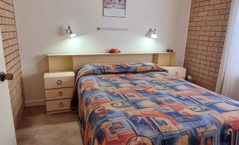 a bed with a colorful quilt is situated in a room with brick walls and two lights on the wall at Lone Pine Motel