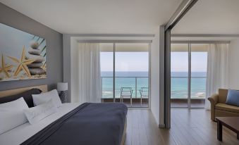 a modern bedroom with a large window offering a view of the ocean , a bed , and white chairs at Resort Hadera by Jacob Hotels