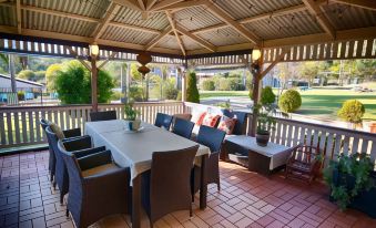 a patio with a dining table , chairs , and a gazebo surrounded by lush greenery and trees at Fairway Motor Inn