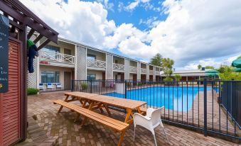 a large outdoor pool surrounded by multiple buildings , with a picnic table and chairs set up next to the pool at Poenamo Hotel