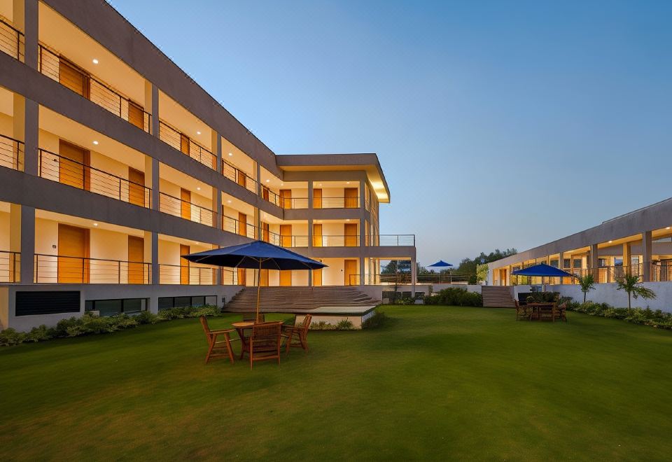 a modern building with multiple balconies and a blue umbrella on the grass near some tables and chairs at Hyatt Place Hampi