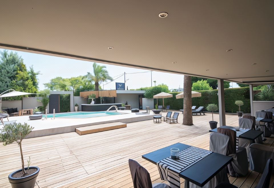 an outdoor patio area with a wooden floor , umbrellas , and tables overlooking a pool and palm trees at Mikelina Boutique Hotel