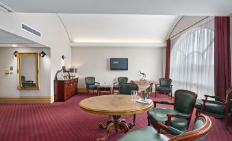 a room with a red carpet and green chairs , a wooden table , and a tv at Hotel Grand Chancellor Launceston