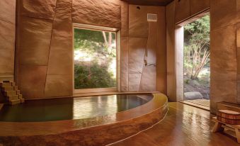 a room with a wooden floor and stone walls has a large window that has trees in the background at Shouen