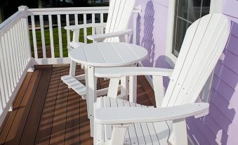 a white adirondack chair and table are sitting on a wooden deck with a purple house in the background at Key West Cottages