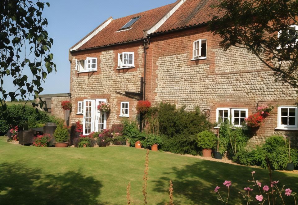 a large brick house surrounded by a lush green lawn , with several potted plants in the yard at Primrose Cottage