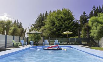 a swimming pool surrounded by trees and umbrellas , with a lifeguard 's chair nearby , under a clear blue sky at North South Holiday Park
