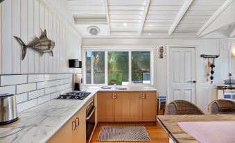 a small kitchen with wooden cabinets and a white tiled floor , featuring a sink , stove , and window at Bear Gully Coastal Cottages