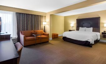 a hotel room with a king - sized bed , an orange couch , and a chair , along with lamps and curtains at Wingate by Wyndham Steubenville