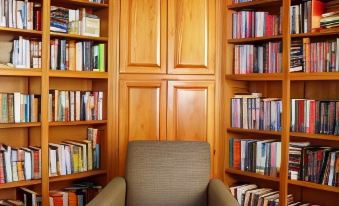 a bookshelf filled with numerous books , with a chair placed in front of it and a wooden door at the end at Finger Lakes Bed and Breakfast