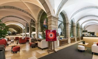 a spacious lobby with high ceilings , stone walls , and large columns , featuring a red archway leading to a reception area at Abbaye de Talloires