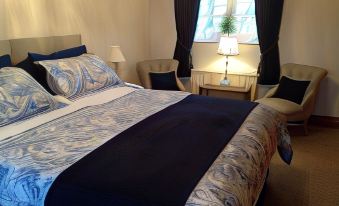 a large bed with blue and white bedding is in a room with a window , lamp , and two chairs at Primrose Cottage