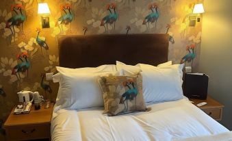 a large bed with white sheets and a brown headboard is positioned under a wall covered in colorful wallpaper at The Ardingly Inn