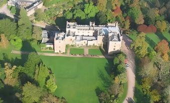 aerial view of a large , castle - like building surrounded by green trees and grass , with a car parked nearby at Irton Hall