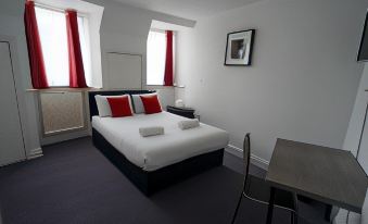 a modern hotel room with a white bed , red curtains , and a tv , along with a desk and a chair at The Bank
