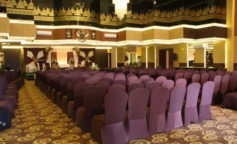 a large conference room with rows of purple chairs arranged in an auditorium - style setting , ready for an event at Tjokro Hotel Klaten
