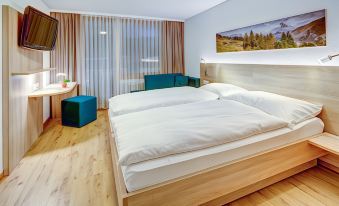 a large bed with white sheets is in a room with wooden floors and a window at Matterhorn Inn