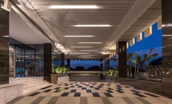 a large , well - lit hotel lobby with a checkered floor and white ceiling , surrounded by potted plants and trees at Neelkanth Sarovar Premiere