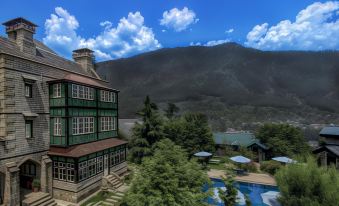 a large green building with a swimming pool in front of it , surrounded by trees and mountains at The Himalayan