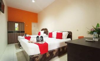 a modern hotel room with two beds , each made up with white sheets and red comforters , surrounded by orange walls and wooden furniture at My Place Guest House Manado