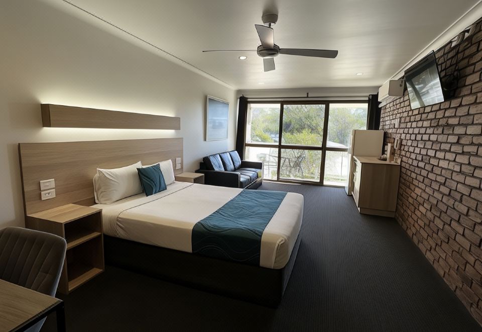 a modern hotel room with a large bed , couch , and sliding glass doors leading to a balcony at Logan City Motor Inn
