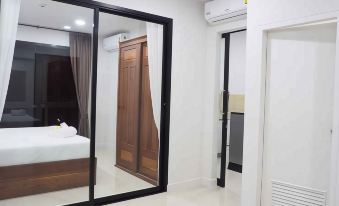 a bedroom with a bed , mirror , and an air conditioner , connected to another room with white walls and brown doors at Klongyai Center