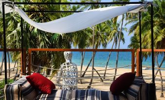 a bed with red and white pillows is situated on a balcony overlooking the ocean at Karpaha Sands