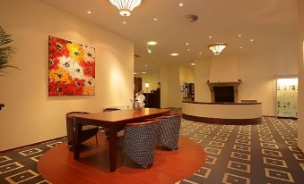 a lobby area with a wooden table and chairs , an abstract painting on the wall , and a fireplace at Fletcher Parkhotel Val Monte