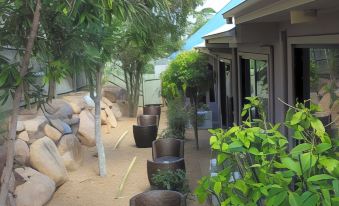 a backyard with a paved walkway , trees , and rocks , surrounded by potted plants and a large tree at Springwood Motor Inn