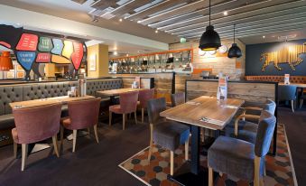 a restaurant with wooden tables and chairs , a counter , and pendant lights hanging from the ceiling at Premier Inn Glasgow (Milngavie)