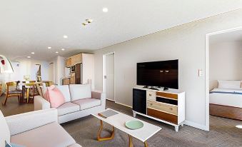 a modern living room with a white couch , pink and gray pillows , wooden coffee table , and a flat - screen tv at Fernz Motel & Apartments Birkenhead