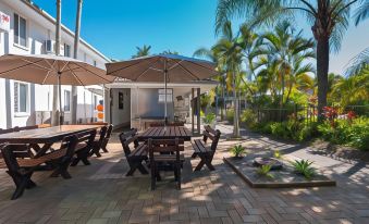 a patio area with a table and benches under a large umbrella , surrounded by palm trees at Bay of Palms