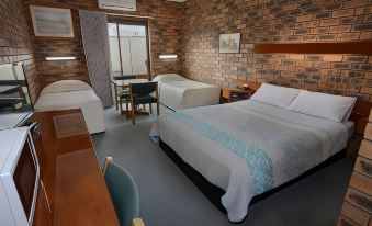 a hotel room with two beds , a dining table , and a brick wall , all decorated in a cozy style at Sandhurst Motor Inn Bendigo