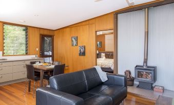 a living room with a black leather couch , wooden walls , and a kitchen in the background at Whispering Valley Cottage Retreat