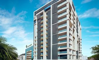 a modern apartment building with multiple floors , surrounded by trees and buildings , under a clear blue sky at Tropics Eight Suites