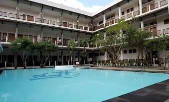 a large swimming pool is surrounded by a modern building with balconies and trees , and a blue tree in the foreground at Laut Biru Resort Hotel