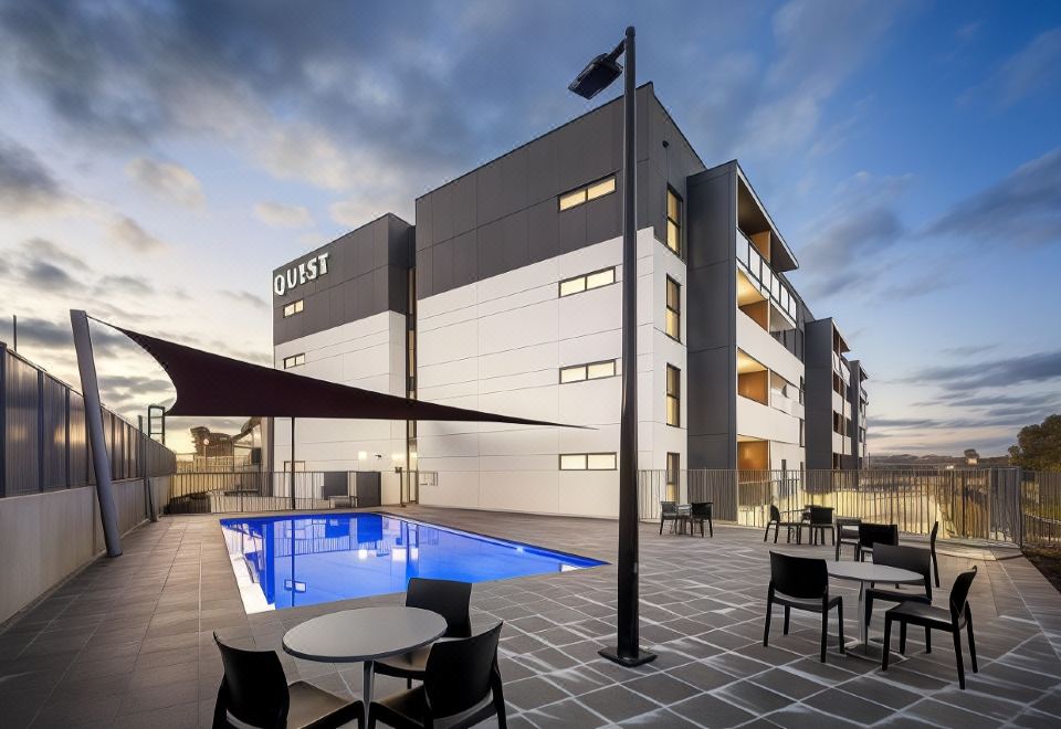 a modern hotel with a swimming pool , outdoor seating area , and umbrellas , under the lights of dusk at Quest Wodonga