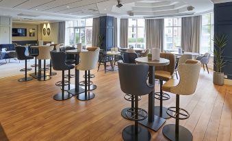 a modern restaurant with wooden floors and chairs , dining tables , and potted plants , all set for dining at Coldra Court Hotel by Celtic Manor