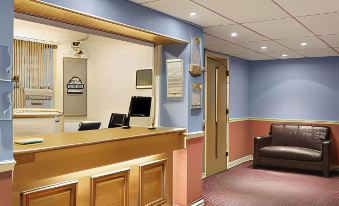 a hotel lobby with a check - in counter , a reception desk , and several chairs arranged around the area at Days Inn by Wyndham Tewkesbury Strensham