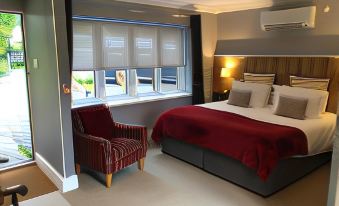 a modern bedroom with a large bed , red comforter , and a red armchair next to a window at The Mill at Glynhir