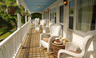 a long , covered porch with white wicker furniture and a tiled floor , providing a relaxing outdoor seating area at Deerhill Inn