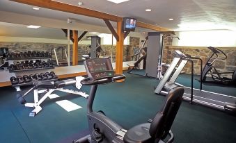 a well - equipped gym with various exercise equipment , including treadmills and weightlifting machines , under a wooden ceiling at The Inn at Montchanin Village