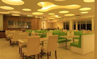 a modern restaurant with green booths and white tables , surrounded by large circular lights on the ceiling at Front One Resort Magelang