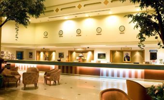 a hotel lobby with a reception desk , two chairs , and multiple clocks on the wall at Thumrin Thana Hotel