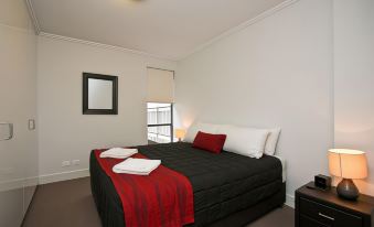 a large bed with a black and red blanket is in a room with white walls at The Star Apartments