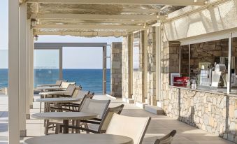 a restaurant patio with outdoor seating , tables , and chairs near the ocean , providing a relaxing atmosphere for guests at Civitel Creta Beach