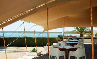 a beach bar with a large canvas tent , white tables and chairs , and a beautiful view of the ocean at Insotel Hotel Formentera Playa