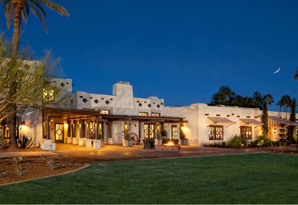 a large , white building with a thatched roof is lit up at night , surrounded by green grass and trees at The Wigwam Resort-Phoenix-Litchfield Park Area