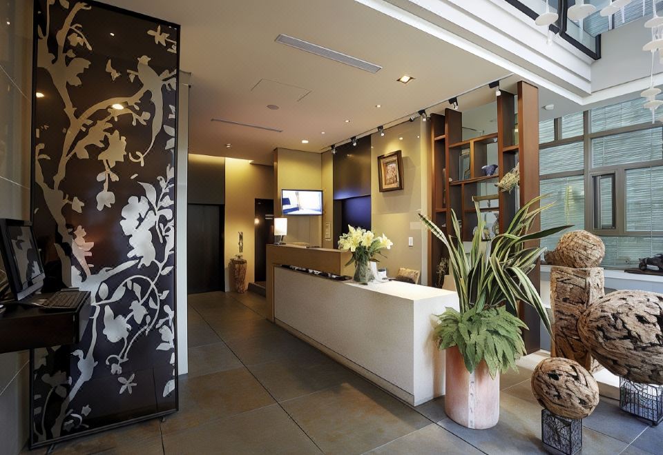a modern office lobby with a white reception desk , two potted plants , and a large screen tv at Micasa Hotel